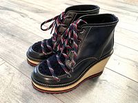 Three-quarters view of Moncler wedge boots showing black leather and shearling upper with multicolor rope laces and beige platform.