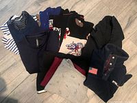 Eight folded sweatshirts and pullovers arranged on light wood floor