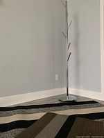 Chrome coat rack with modern design and round base against a wall.