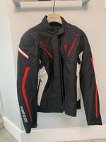 Front view of black, red and white jacket showing zip closure, chest pocket and logo