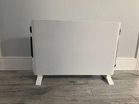 Side view of the white rectangular Delonghi convection panel heater standing on feet, plugged in with the power cord visible.