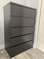 Front view of the tall dark brown IKEA chest of drawers showing two smaller top drawers and three larger lower drawers.