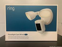 Front view of the box showing the Ring Floodlight Cam Wired Pro with dual floodlight heads and camera unit in white.