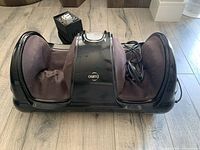 Front and side angled view of the Osim foot massager on a wood floor alongside the power converter.