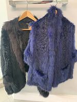 Black fur jacket with textured body and dark fur trim hanging next to indigo blue reversible fur vest.