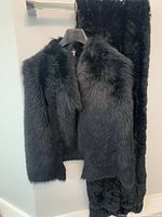 Black fox fur vest with dense fur texture and black rabbit fur shawl hanging together on a hanger and rack.