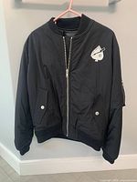 Full front view of black bomber jacket showing zip closure and flap pockets