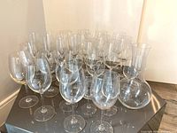 28 clear glass wine glasses and 1 glass decanter arranged on a black surface showing the full lot.