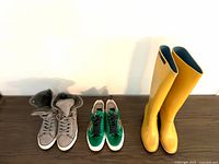 Three pairs side by side: gray suede high-top with fur lining (left), green low-top sneakers (center), yellow rain boots (right).