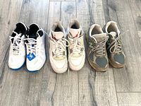 Three pairs of ladies trainers: Victor badminton shoes, white with blue sole and black lining; Air Jordans white with red logo; New Balance 2002R multi-color.