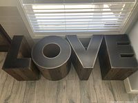 Front view showing four side tables spelling out 'LOVE' under window blinds.