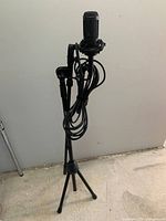 Photograph of the full microphone setup showing the microphone mounted on the adjustable tripod stand with the cable wrapped around the stand.