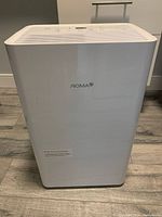 Front view of white NOMA dehumidifier unit standing on floor, showing logo and overall design.