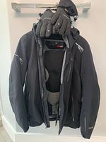 Black Spyder men's small ski jacket hanging on a hanger showing front with gloves on top.