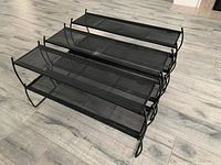 Three black metal mesh stackable shoe racks arranged on floor.