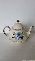 Front view of the ivory ceramic Sadler teapot with blue floral design, gold accents on lid and handle, shiny surface visible.