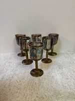 Set of six brass mini goblets with abalone shell inlay on the cups, arranged and photographed against a neutral background to highlight the colors and details of the shell and brass.