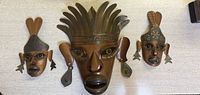 Front view of three vintage handmade Mexican folk art wooden masks arranged on a light surface.