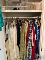 Closet rod with various garments hanging including dresses, sweaters, jackets, and blouses in different colors and patterns.