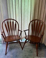 Two Ercol Windsor armchairs placed side by side, showing front and side angles against a curtain background.