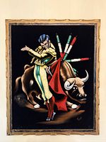 Framed black velvet painting showing a matador with yellow and green attire and a bull with decorated back, holding a red cape in front of the bull, signed by the artist.