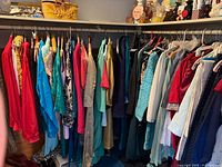 Wide shot of master closet racks with assorted women's clothing hung, showing variety of colors and garment types.