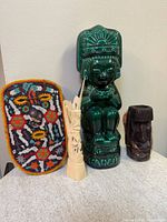 Four vintage cultural collectible items displayed together: green pottery decanter with Mayan Aztec styling, carved ivory tone figurine, dark wooden carving, and Mexican Huichol beadwork mask.
