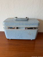 Closed light blue Samsonite Profile train case with metal trim and handle on a wooden surface.