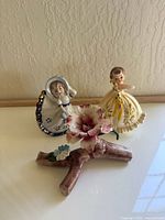 Top view of two girl figurines standing behind a porcelain floral branch with pink and white flowers on a branch marked Capodimonte.