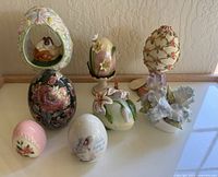Full display of nine distinct vintage ceramic decorative eggs on a smooth surface viewed from above.