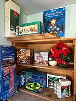 Photo of wooden shelving filled with various vintage Christmas decorations including boxed candy canes, multiple boxed snow globes, a poinsettia floral arrangement, and several boxed holiday light sets.