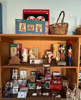 Full view of wooden shelves containing a variety of vintage Christmas decorations including nutcrackers, Santa figurines, boxed ornaments, and related holiday items with an empty basket on top shelf.