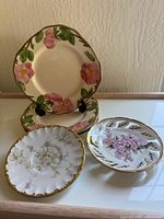 Three decorative plates arranged on glass surface, two with Franciscan Desert Rose pattern and one smaller floral plate