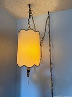 Side view of swag lamp showing scalloped cylindrical beige fabric shade and brass suspension chain.