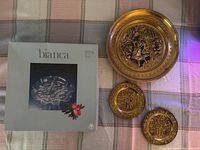 Set of three brass plates on a plaid cloth, with box labeled 'bianca' visible