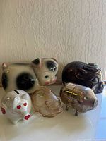 Five piggy banks on display including varied materials ceramic, glass, metallic
