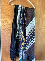Lot of 4 vintage scarves hanging on a hanger showing different patterns including solid black, floral, and geometric designs.