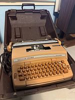 Vintage Smith-Corona Coronet Super 12 electric tan typewriter in its open hard plastic brown carrying case showing the keyboard and body.