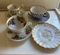 Photo showing three vintage teacups and saucers with distinct floral and fruit patterns and gold trim detailing on a tray.