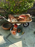 Photo of vintage rusty metal wheelbarrow holding various terra-cotta pots and two decorative metal sun ornaments with garden background