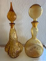 Front view of two vintage amber Italian Empoli glass decanters with distinct stoppers and grape cluster / floral designs.