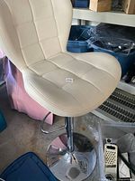 Beige adjustable height bar stool with padded seat and backrest, chrome base, and footrest, shown from side angle.