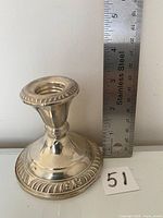 Front view of silver candle holder, showing detailed rope-like ornamental rim and polished finish with ruler for scale.