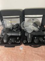 Two Wotime V12 massage guns each in its own black hard carrying case with five massage heads and charging cables.