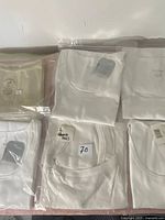 Photo showing six packaged ladies blouses, mostly white, sealed in clear plastic bags with tags and stickers.