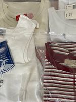 Six ladies blouses displayed in plastic packaging showing variety of white tops and striped blouses with tags attached.