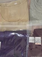 Close-up photo showing beige ribbed blouse and grey blouse along with purple blouse in plastic bag