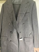 Gray double-breasted suit jacket hanging, showing front with six buttons, two front flap pockets, one chest pocket, and notch lapels.