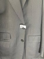 Close-up of the front of the men's suit jacket showing the lapel, buttons, and flap pockets with a size tag marked 65.