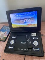 Portable DVD player open showing the screen with setup menu and control buttons, with DVD case visible to left